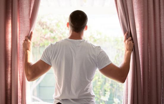 I love when the sun is out to greet me. Shot of a young man opening his curtains to a bright sunny morning.