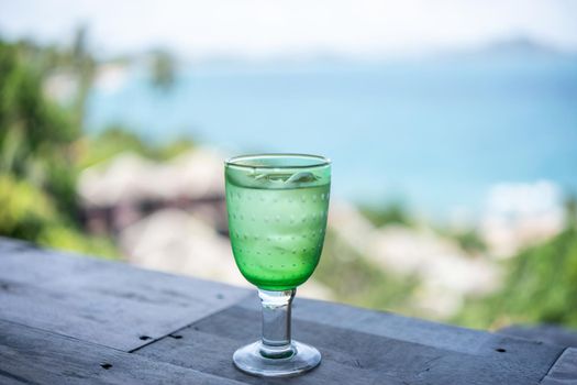 Glass of drinking water with ice over blur ocean background.