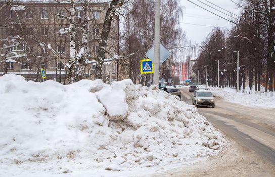 A huge large snowdrift by the road against the backdrop of a city street