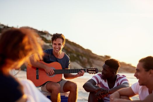 Friends are the ones who inspire and motivate us. Shot of a man playing the guitar while sitting on the beach with his friends.