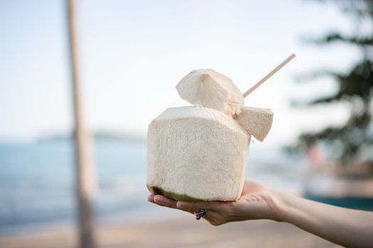 Fresh coconut cocktail in hand over ocean background.