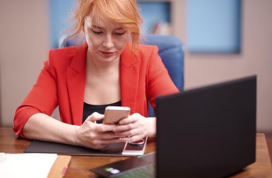 Businesswoman using smartphone and laptop while working at the office