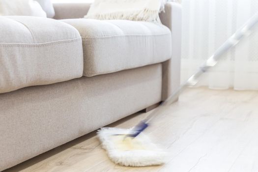Cleaning floor with white mop near sofa
