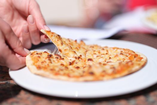 Female hand tearing off appetizing hot slice of pizza with cheese closeup