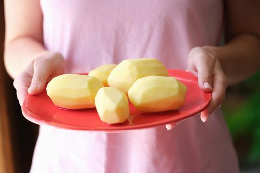 Woman housewife holding plate of peeled potatoes in her hands closeup