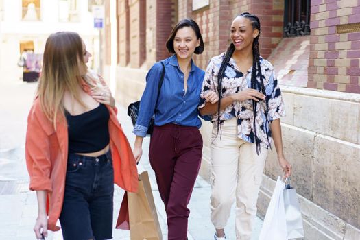 Smiling diverse women with shopping bags walking on street