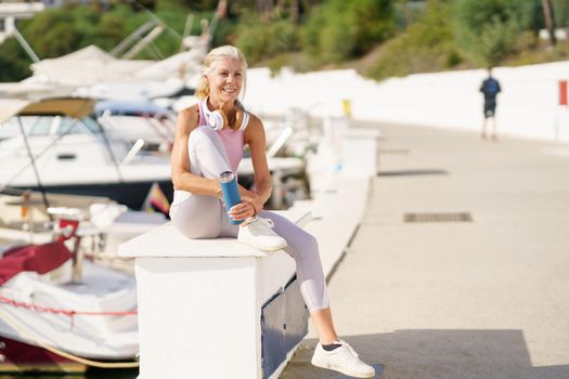 Senior woman taking a break during exercise to hydrate herself. Mature female in fitness clothing drinking water from a metal fitness bottle. Concept of healthy living in the elderly.