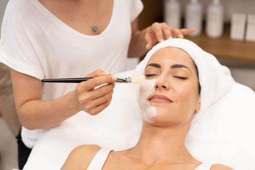 Aesthetics applying a mask to the face of a Middle-aged woman in modern wellness center.