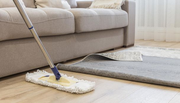 Cleaning floor with mop under carpet in living room