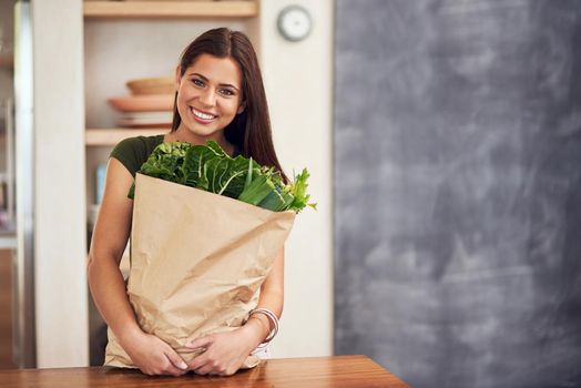 As fresh as it gets. Portrait of an happy young woman holding a bag of groceries in her kitchen.