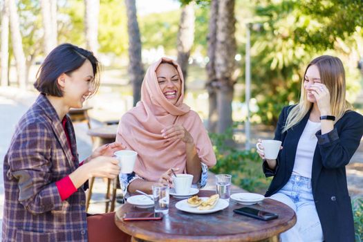 Cheerful multiracial women sitting in outdoor cafe