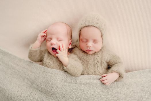 Twins newborn babies sleeping wearing knitted costumes and yawning studio portrait. Siblings brothers infant children napping together