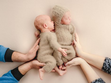 Parents hands holding twins newborn babies during children sleeping. Infant siblings brothers napping with mother and father