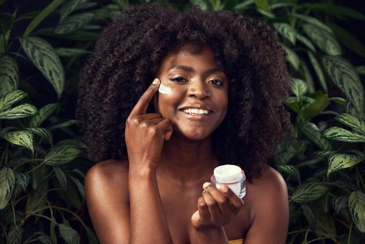 The less chemicals, the happier my skin. Shot of a beautiful young woman applying moisturiser to her face against a leafy background.