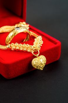 Gold necklace and heart shape pendant and gold ring in red velvet box on black.