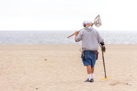 LOS ANGELES, CALIFORNIA, USA - 11 MAY, 2019: Man with metal detector on Venice beach in Los Angeles searching for lost jewellery and coins.