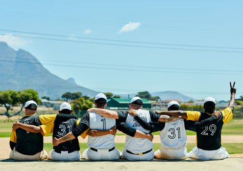 First baseball, then peace. Rearview shot of a team of unrecognizable baseball players embracing each other while sitting near a baseball field during the day.