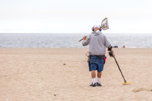 LOS ANGELES, CALIFORNIA, USA - 11 MAY, 2019: Man with metal detector on Venice beach in Los Angeles searching for lost jewellery and coins