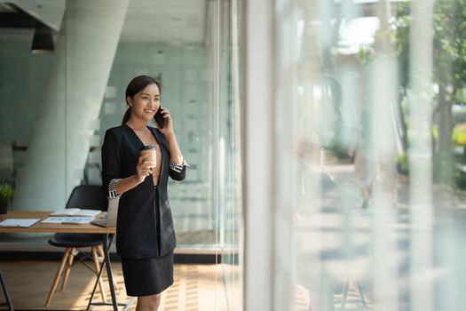 Asian business woman making a phone call and smiling at modern office