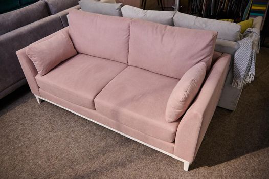 High angle view of a stylish pink settee with cushions in the showroom of upholstered furniture. Furniture store