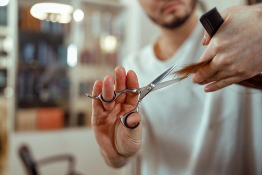 Closeup of hairdresser hands holding scissors and cutting client hair