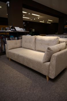 Stylish comfortable sofa with cushions near a stand with fabric samples for upholstery in the showroom of furniture store. Living room furnishing with stylish modern comfortable upholstered furniture