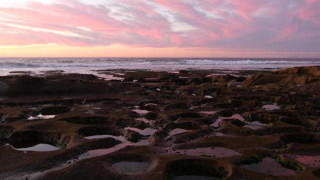 Eroded tide pool rock formation in California. Sunset sky reflection in water.