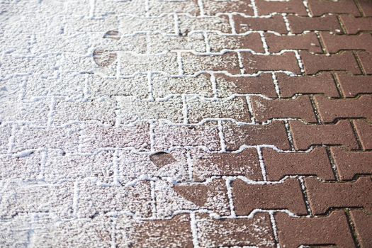 Partially snow-covered red cobblestone sidewalk. Close-up view.