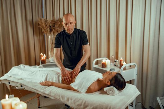 Alternative medicine male therapist doing massage to female client lying on a daybed