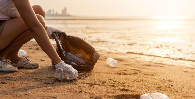 Volunteer woman picking plastic bottle into trash plastic bag black for cleaning the beach