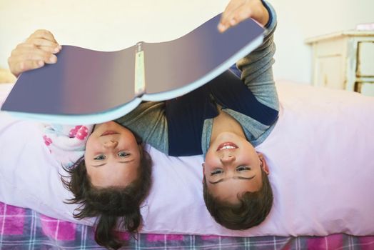 They share a love for reading. Cropped shot of two young siblings reading a book together while lying upside down on a bed.