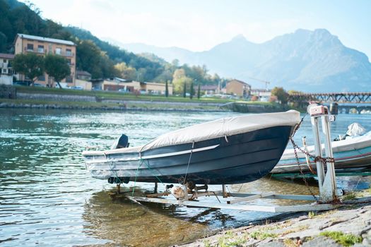Docked boats on the lake Como district in Italy on sunny day. Alp mountains on background. Lecco, Italy - October 17, 2020