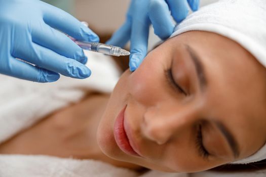 Closeup of young woman receiving hyaluronic acid injection in cheekbones at beauty salon