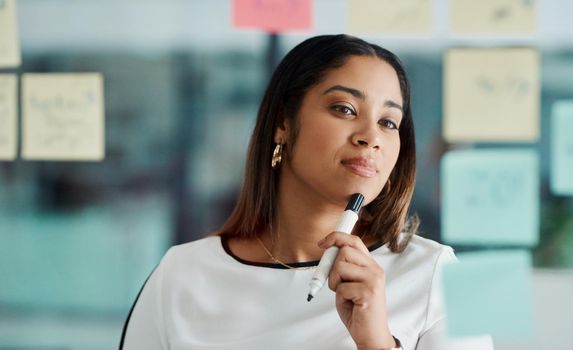 Brainstorming improves your critical thinking and problem-solving skills. Shot of a young businesswoman brainstorming with notes on a glass wall in an office.
