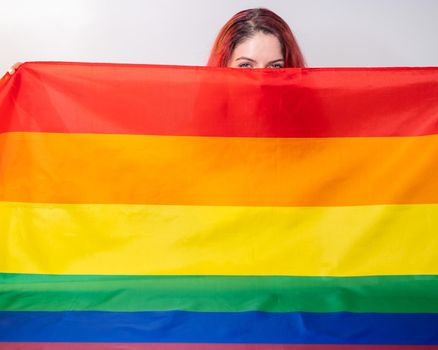 Caucasian woman holding lgbt flag covering herself.