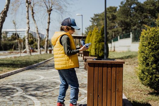 Schoolboy kid throwing the trash into dumpster. Boy using recycling bin to throw away the litter. Caucasian child recycles the junk into the trash-can