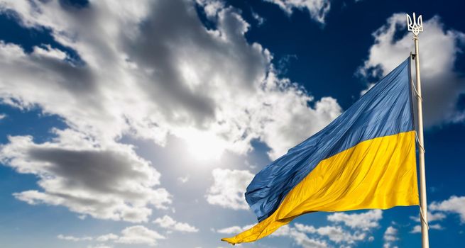 Large national flag of Ukraine flies in the blue sky. Big yellow blue Ukrainian state banner. Independence, flag, Constitution Day, National Holiday, text space.