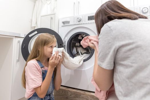Happy family mother housewife and child daughter in laundry with washing machine