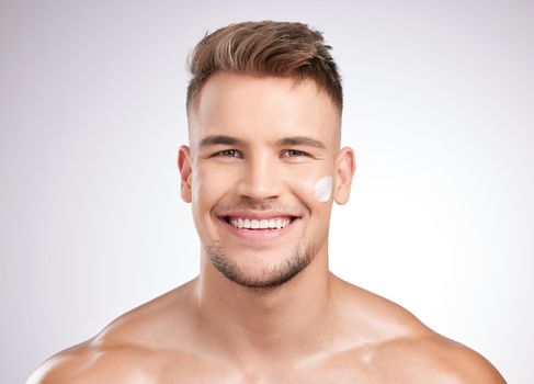 It works like a dream. Studio shot of a young man applying moisturizer to his face against a grey background.