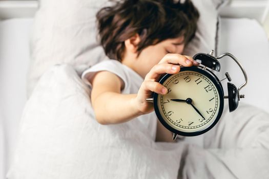 Boy holding alarm clock showing quarter past seven
