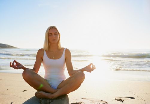 Namaste right here. Full length shot of an attractive young woman sitting with her legs crossed and meditating on the beach.