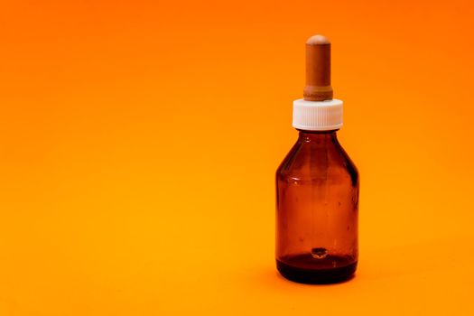 Small bottle with amber glass dropper insulated on orange background.