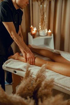Concentrated male therapist doing professional leg massage for female client at spa center