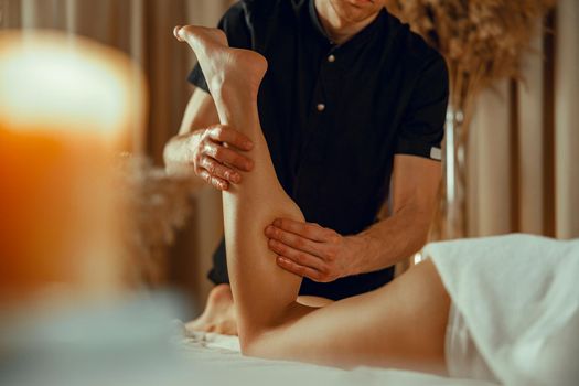Male therapist doing professional leg massage for female client at spa center
