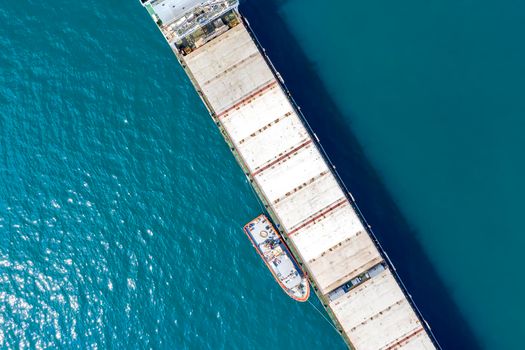Aerial shot of a cargo ship approaching port with help of towing ship