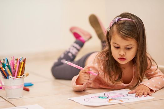 Getting comfortable to get creative. Shot of a little girl colouring in a picture at home.