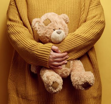 woman in orange knitted sweater hugs cute brown teddy bear. The concept of loneliness and sadness, depression