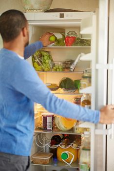 His fridge encourages healthy eating. Rearview shot of a man opening a fridge filled with healthy food at home.