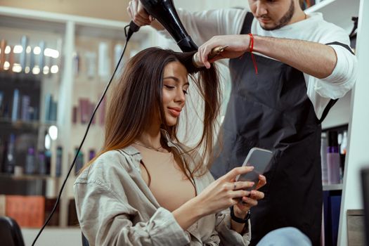 Beautiful woman with long hair using smart phone at beauty salon