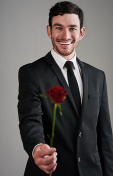 The perfect gentleman. Studio shot of a well-dressed man holding a red rose against a gray background.